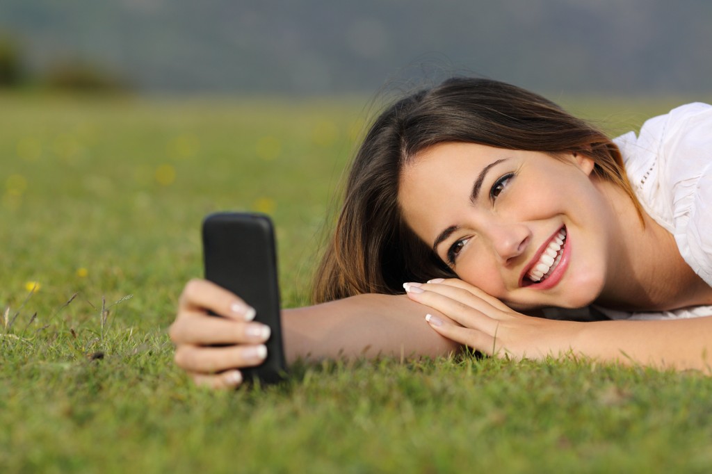 Girl-with-straight-teeth-lying-on-grass-taking-a-selfie